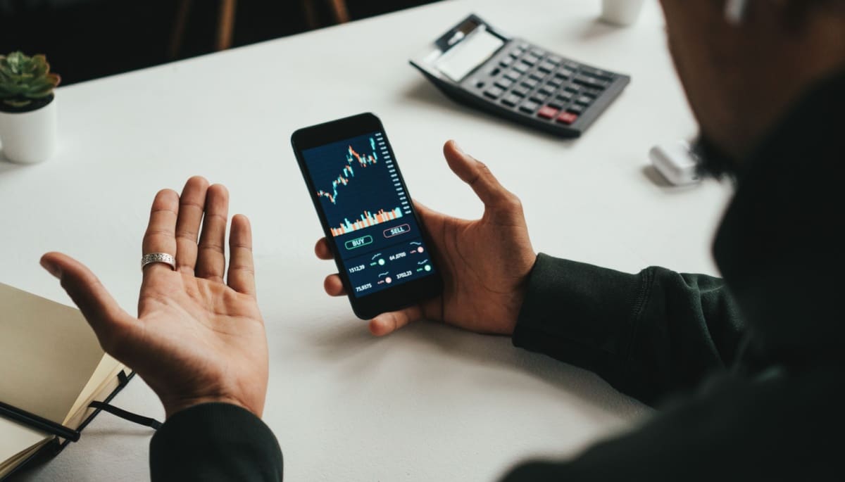 Man trading grafiek telefoon bureau Duizenden Nederlanders verdienen 114% met gratis ‘crypto-supercomputer’