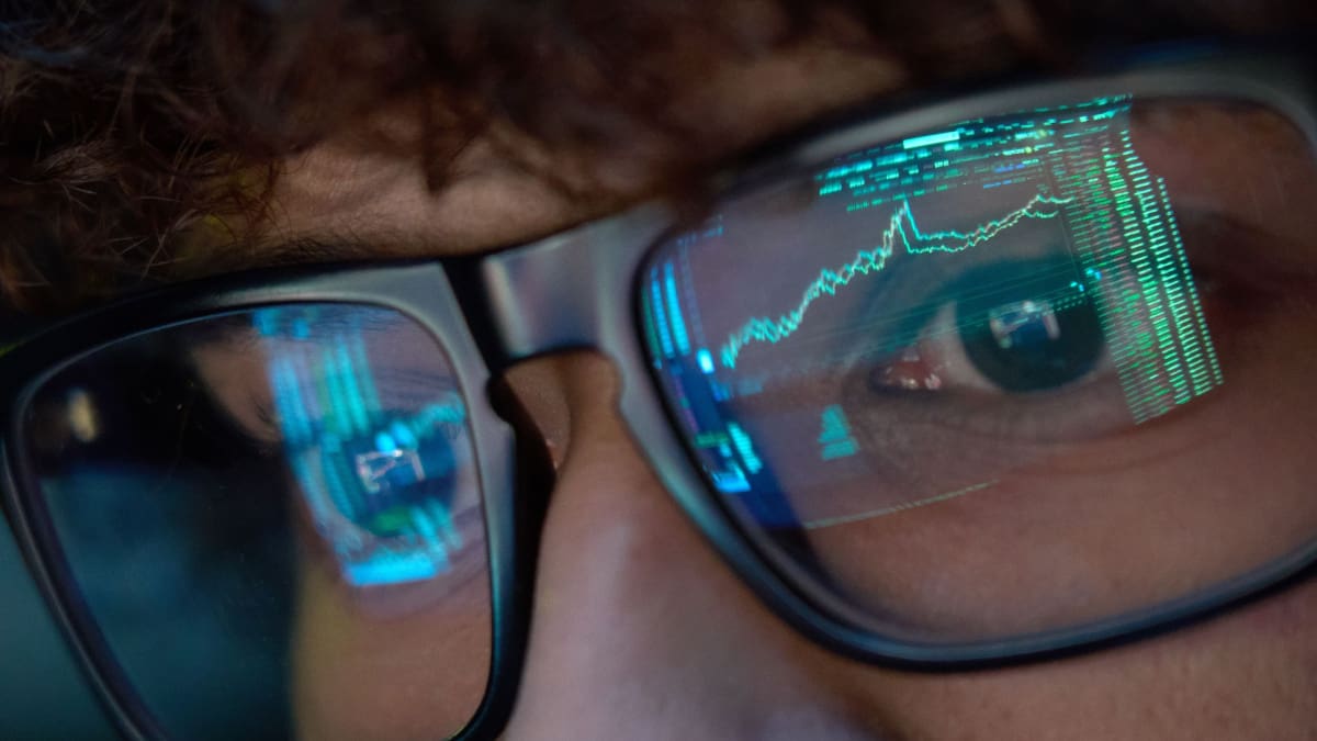 Een close up afbeelding van een crypto handelaar met koersen en grafieken van een cryptobeurs als weerspiegeling op zijn bril Een close up afbeelding van een crypto handelaar met koersen en grafieken van een cryptobeurs als weerspiegeling op zijn bril